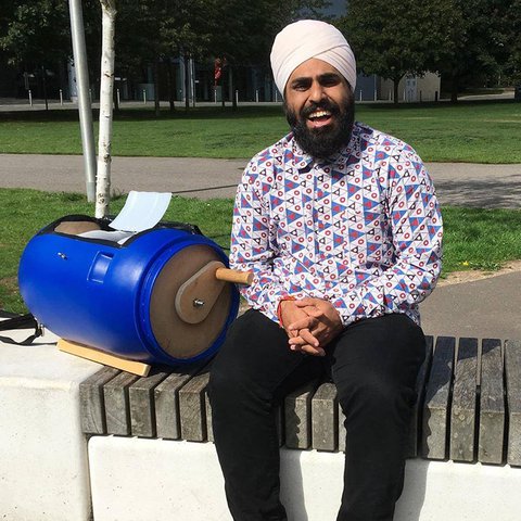 Nav sitting on a wall with his bright blue hand-cranked washing machine next to him, which looks like a blue tombola