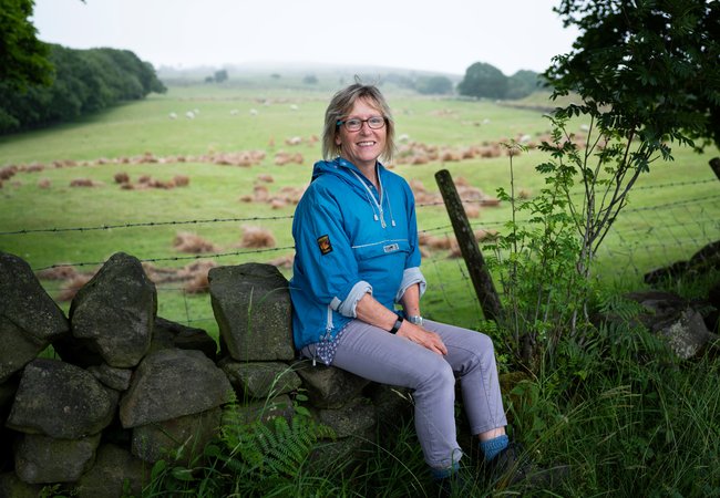 Nicky, Legacy pledger and Oxfam supporter, sits smiling on a dry stone wall.