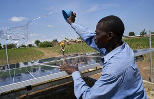 Joshua throws water over the community solar panels to clean them