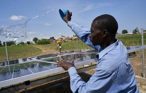 Joshua throws water over the community solar panels to clean them