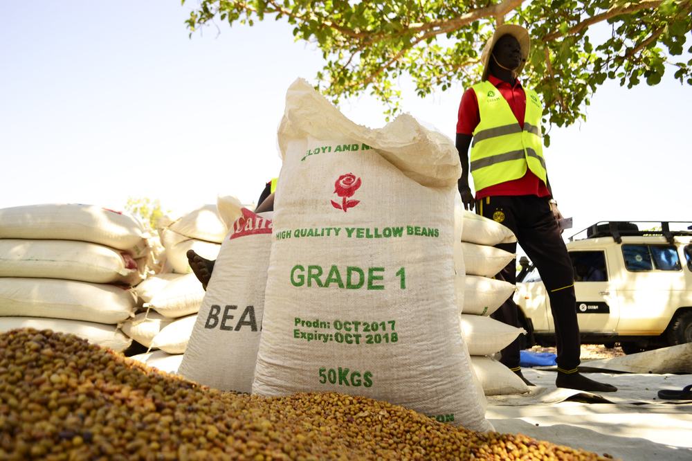 An Oxfam worker stands next to a bag stamped high quality yellow beans
