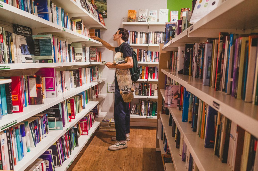 Lewis, 19, holds a skateboard and browses books in the Oxfam Books and Music Shop in Chorlton.