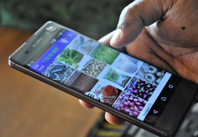 A picture of a mobile phone in a hand with photos of vegetables on the screen