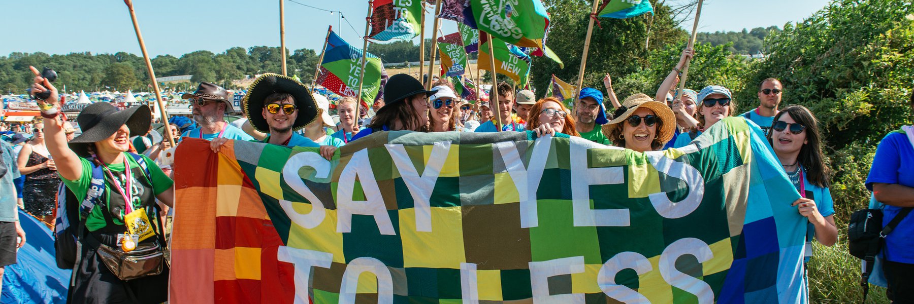 A group of volunteers stand by a patchwork banner that says 'say yes to less'
