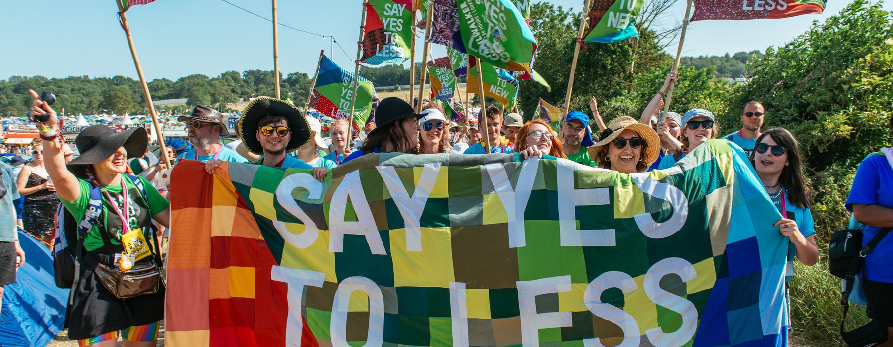 A group of volunteers stand by a patchwork banner that says 'say yes to less'