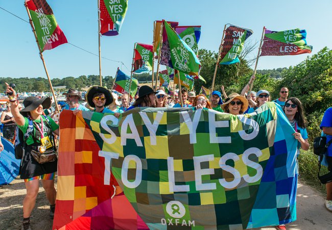 A group of volunteers stand by a patchwork banner that says 'say yes to less'