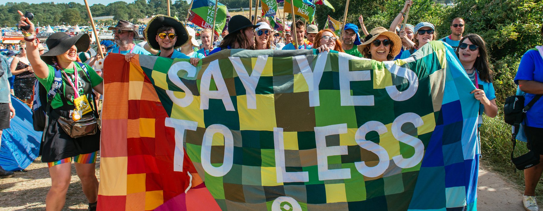 A group of volunteers stand by a patchwork banner that says 'say yes to less'