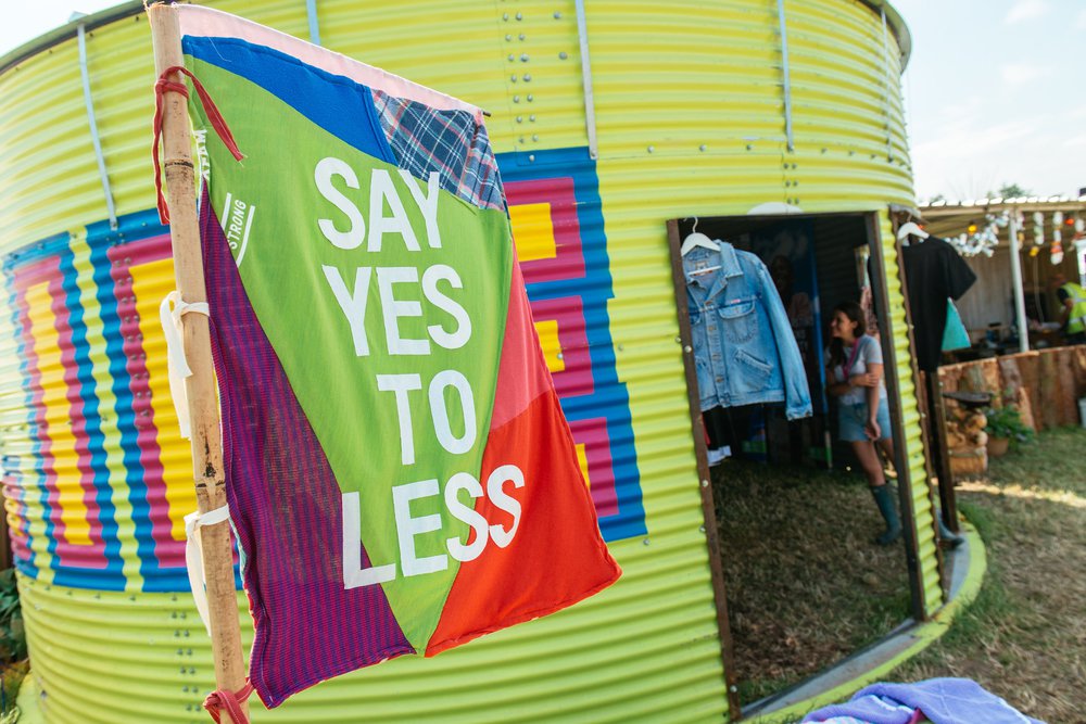 A patchwork say yes to less banner flies in front of a pained Oxfam water tank at a festival