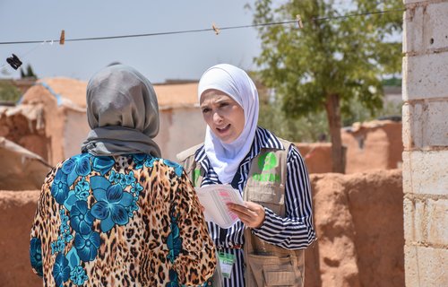 Sana wears a white hijab and Oxfam vest as she talks with a person in Rural Aleppo.