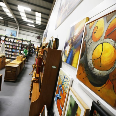 Yellow abstract paintings on the wall of the Oxfam superstore with second hand furniture in the background.