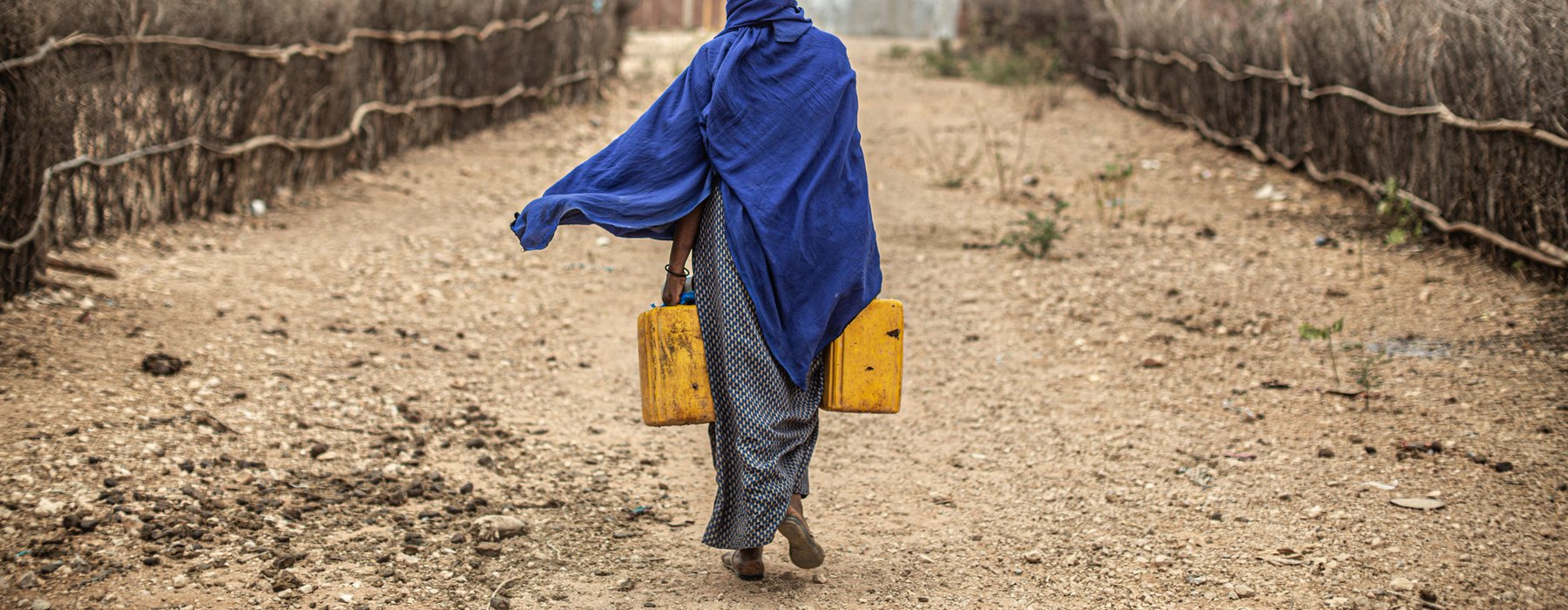 Amina in Ethiopia walks away down an arid path with two water containers. Image: Pablo Tosco/Oxfam Intermon