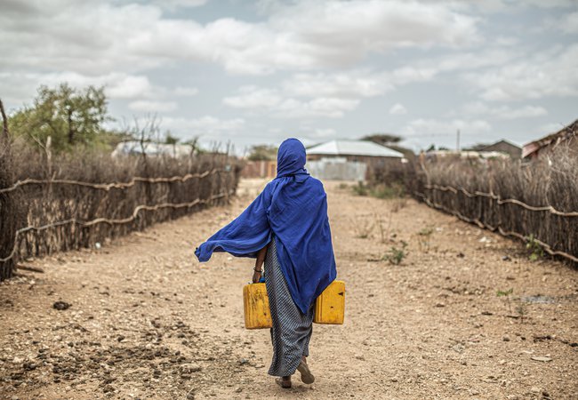 Amina in Ethiopia walks away down an arid path with two water containers. Image: Pablo Tosco/Oxfam Intermon