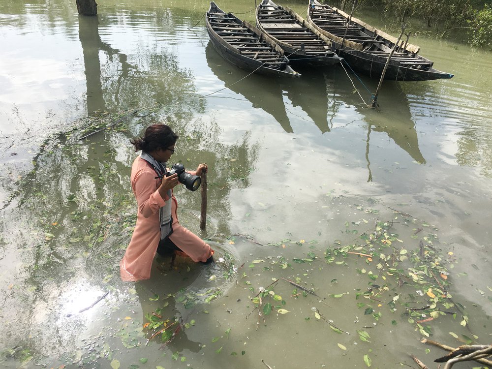 Fabeha Monir wades through floodwater in Bangladesh holding a camera