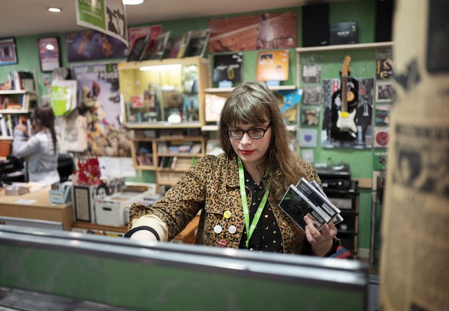 Music shop volunteer, Lucy, arranges CD display in Oxfam music shop, Byres Road, Glasgow