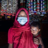 A woman wears a surgical mask and holds her baby in the Cox's Bazar refugee camp
