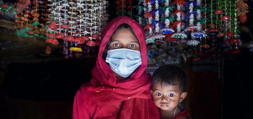 A woman wears a surgical mask and holds her baby in the Cox's Bazar refugee camp