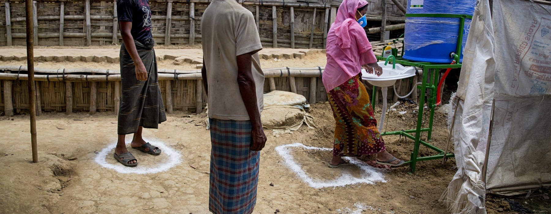 Three people stand in social distancing spray painted circles on the ground near a tap