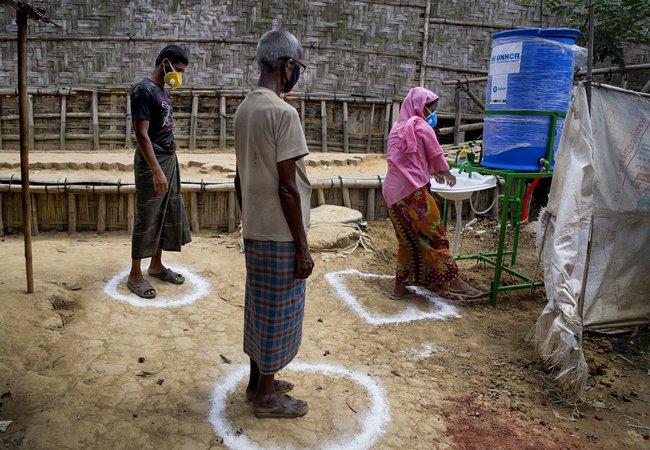 Three people stand in social distancing spray painted circles on the ground near a tap