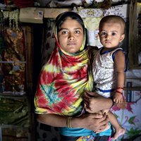 Hafeza stands with her toddler in her makeshift home in the refugee camp