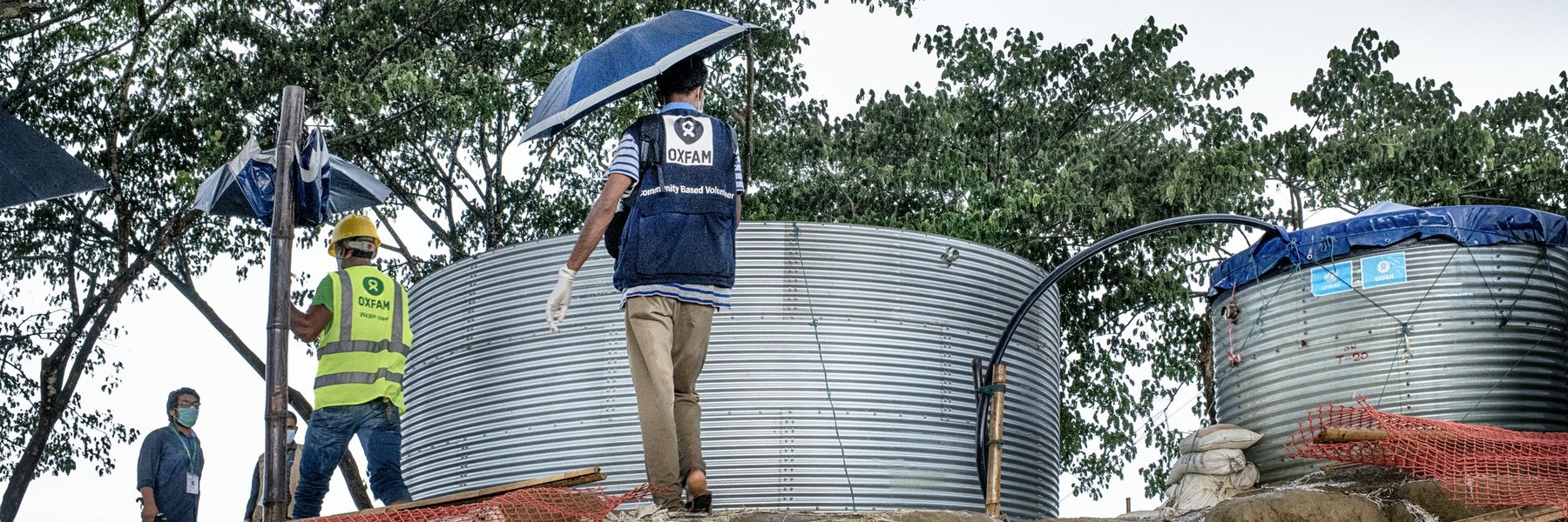 Two men walk past two water tanks holding umbrellas