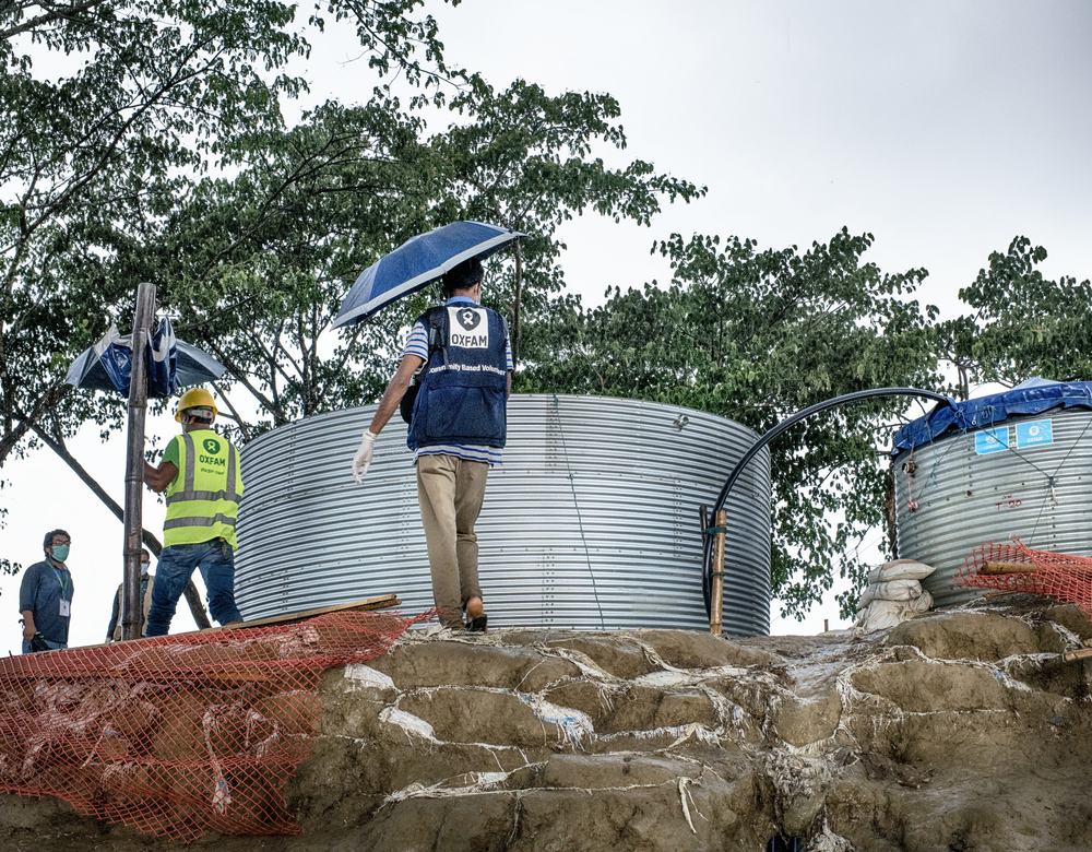 Two men walk past two water tanks holding umbrellas