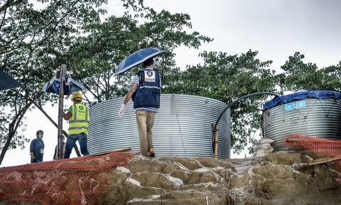 Two men walk past two water tanks holding umbrellas