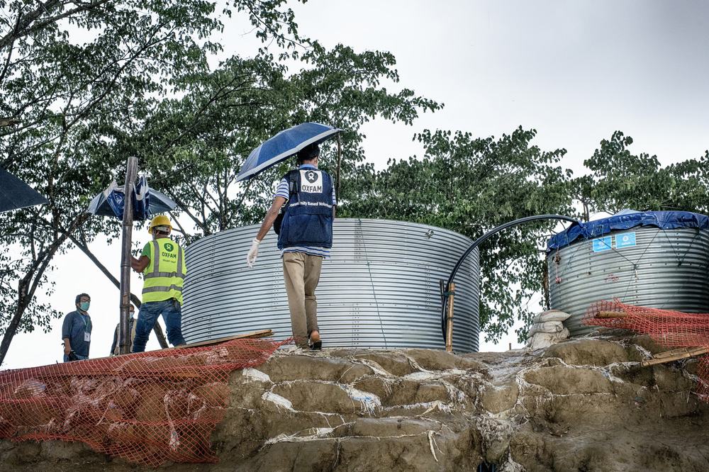 Two men walk past two water tanks holding umbrellas
