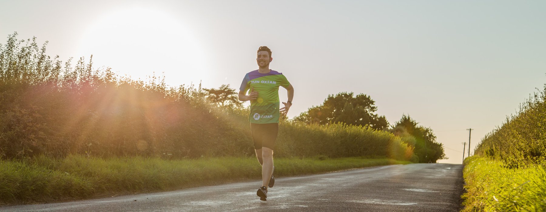 Runner Olly wearing Oxfam shirt training on road by fields.