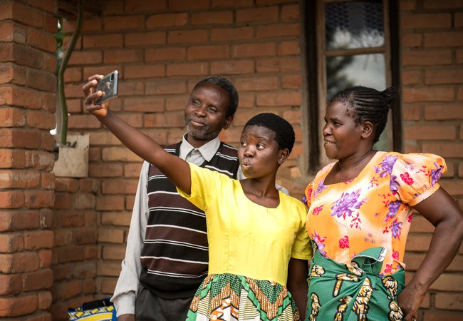 Jessy has fun pouting at a phone camera as her parents stand either side of her smiling