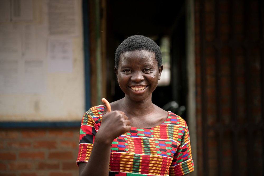 Jessy wears a brightly coloured dress. She's giving the thumbs up.