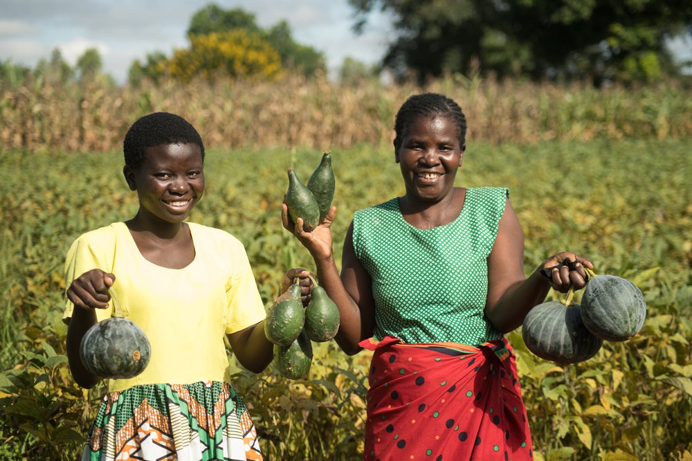 Jessy and her Mum stand in a field holding some crops they have grown and smile