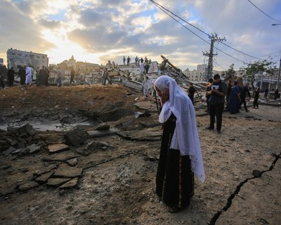 Gaza city after heavy night of Israeli warplanes bombing. A woman walks in the foreground with a hand to her head.