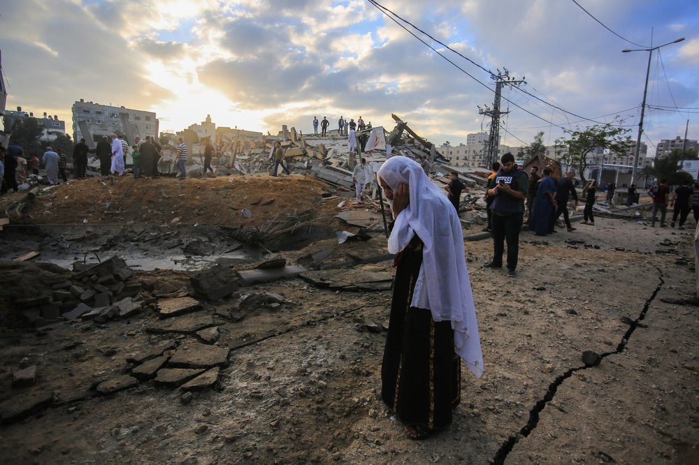 Gaza city after heavy night of Israeli warplanes bombing. A woman walks in the foreground with a hand to her head.