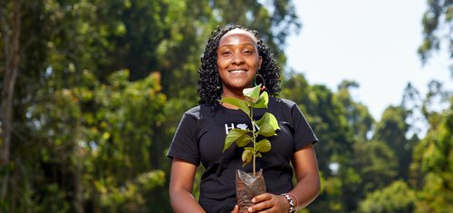 Climate activist and youth leader Elizabeth holds a sapling outside and smiles