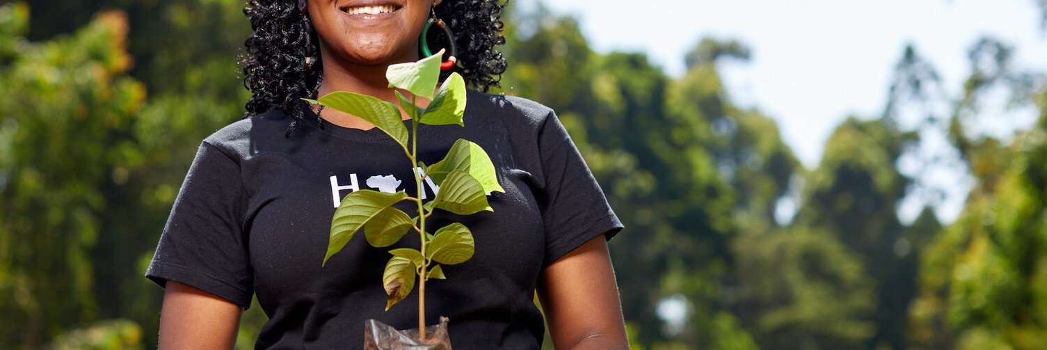 A young woman holds up a tree sapling as part of a school tree planting initiative in Kenya.