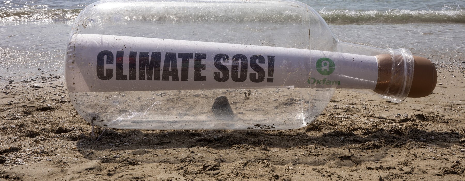 A giant bottle with a message that says Climate SOS and an Oxfam logo stit on the shoreline in Cornwall