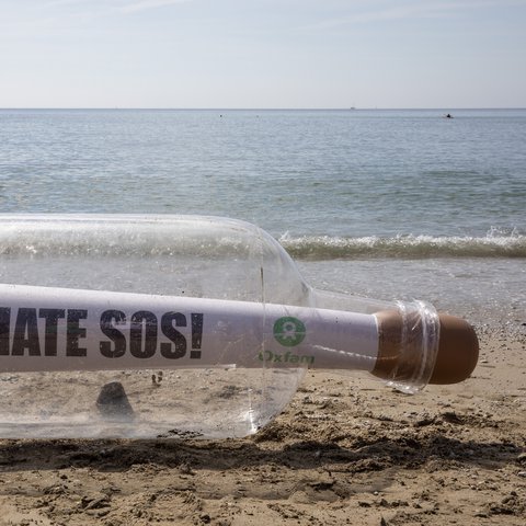 A giant bottle with a message that says Climate SOS and an Oxfam logo stit on the shoreline in Cornwall