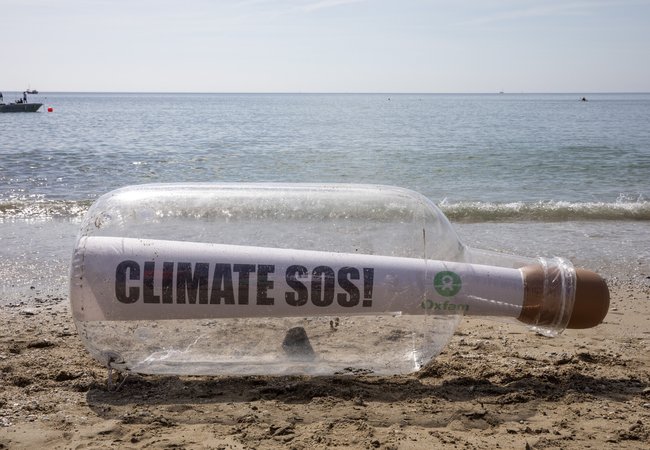 A giant bottle with a message that says Climate SOS and an Oxfam logo stit on the shoreline in Cornwall