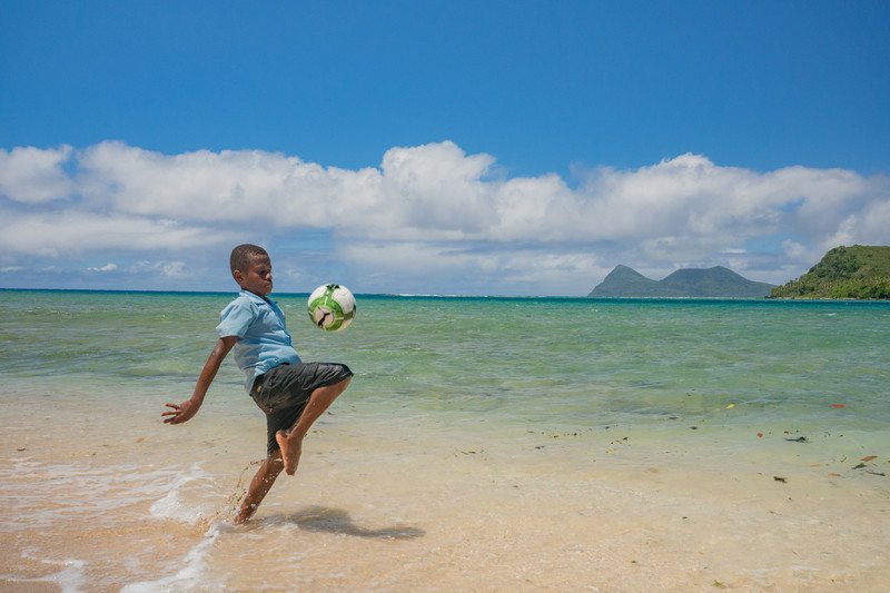 A boy in Vanuatu plays football in the waves, where there was once a playing field.