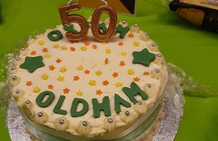 A white cake with green letters that say '50 Oldham'