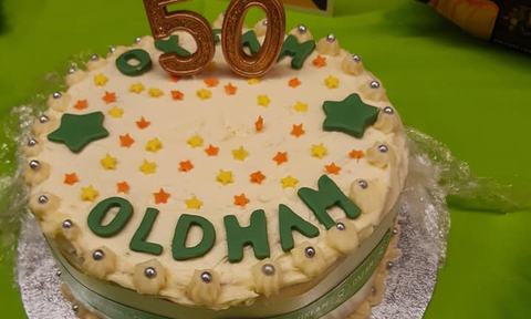A white cake with green letters that say '50 Oldham'