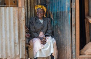 Weremasia Osebe sits at her stall in Kibarage, Nairobi, Kenya with food sitting in baskets in front of her