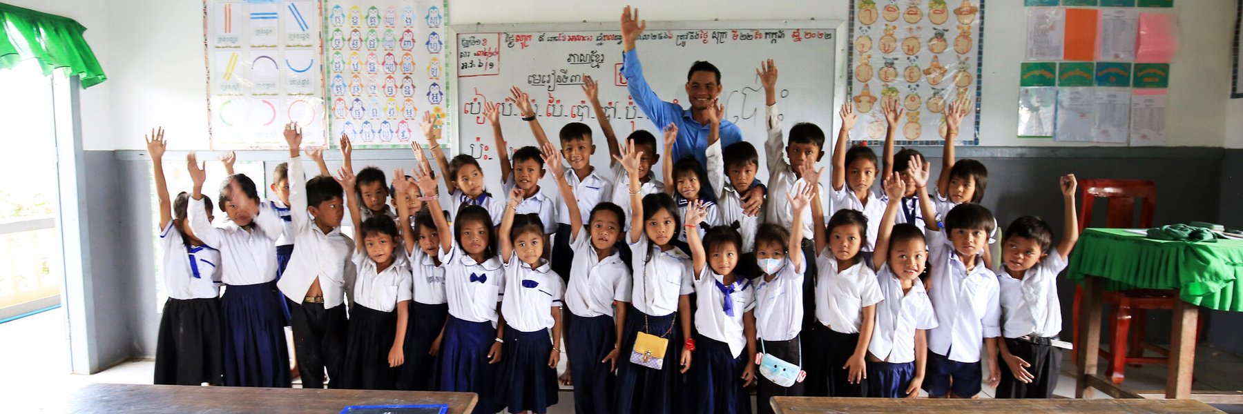 A class of children smile and wave in their classroom in Tonle Sap Lake, Cambodia.