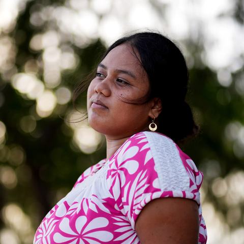 A woman looking into the distance, with greenery in the background.