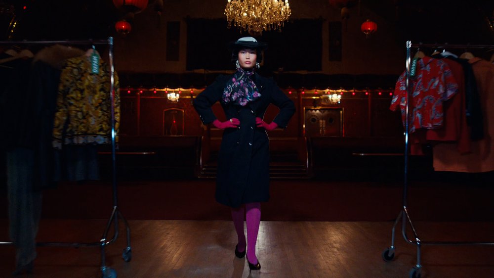 An Asian model in her early 20s wearing a white and navy smart hat and a military inspired navy wool coat and lilac tights. She also wears a floral silk scarf.