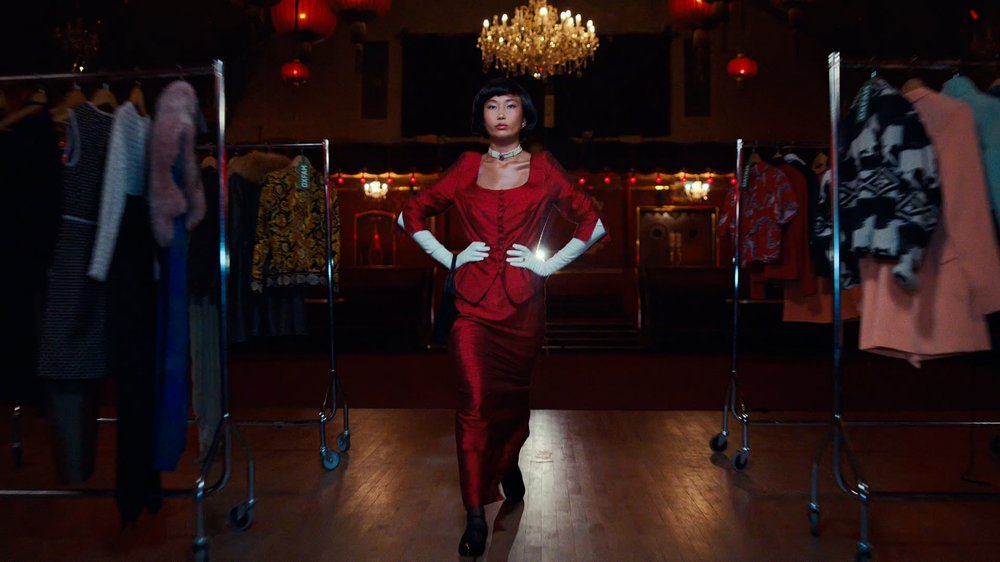 An Asian model in her early 20s wears a red dress and top combo with long sleeved white gloves.