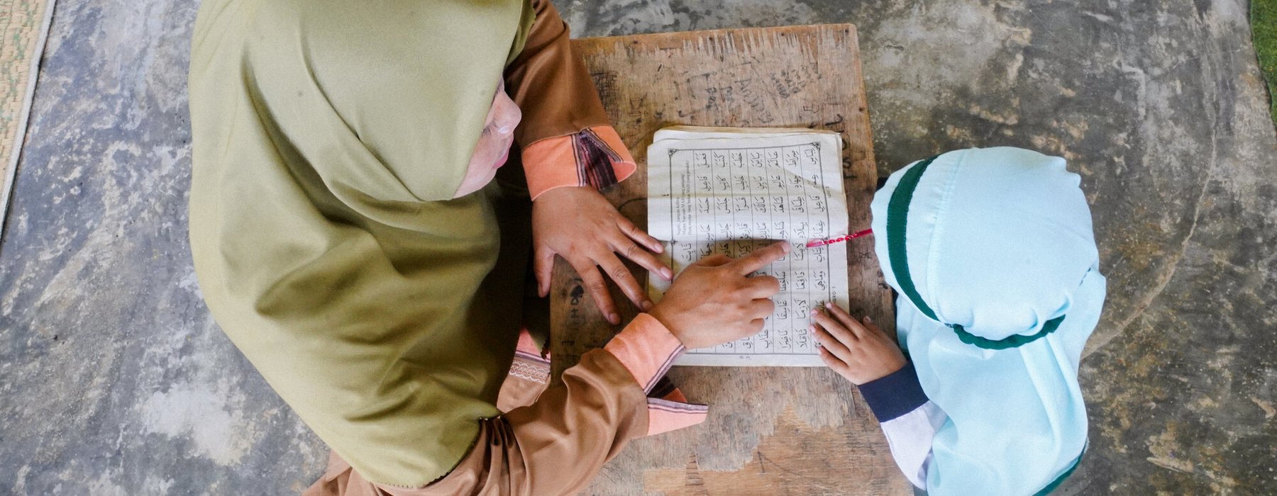An overhead shot of a woman teaching a small child from a textbook in Lombok Timur, Indonesia.