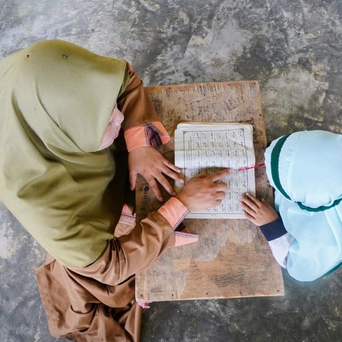 An overhead shot of a woman teaching a small child from a textbook in Lombok Timur, Indonesia.