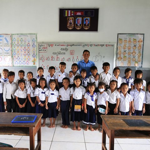 Teacher Vuthy proudly posing in front of the class with his first grade students in Tonle Sap Lake, Cambodia.