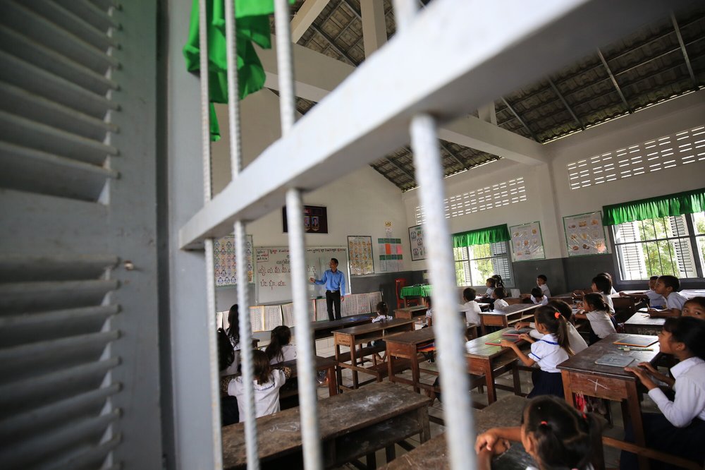 A classroom of primary school children in Cambodia who watch attentively as their teacher points to a blackboard.